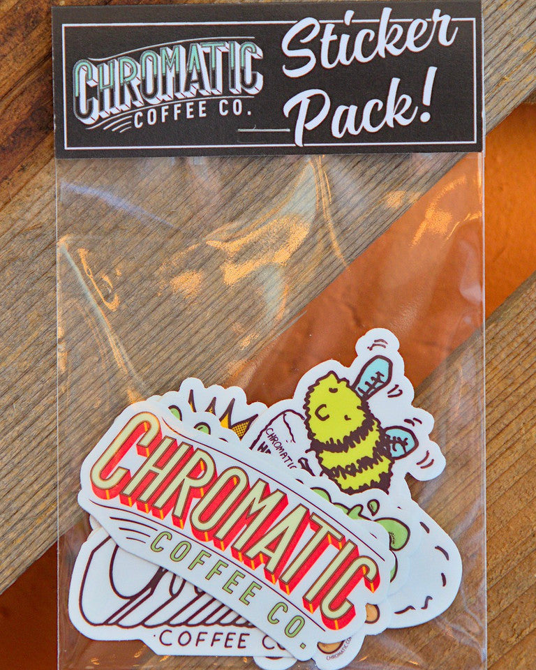 A sticker pack from Chromatic Coffee Co. displayed on a wooden surface, including various stickers with coffee-related illustrations and text.