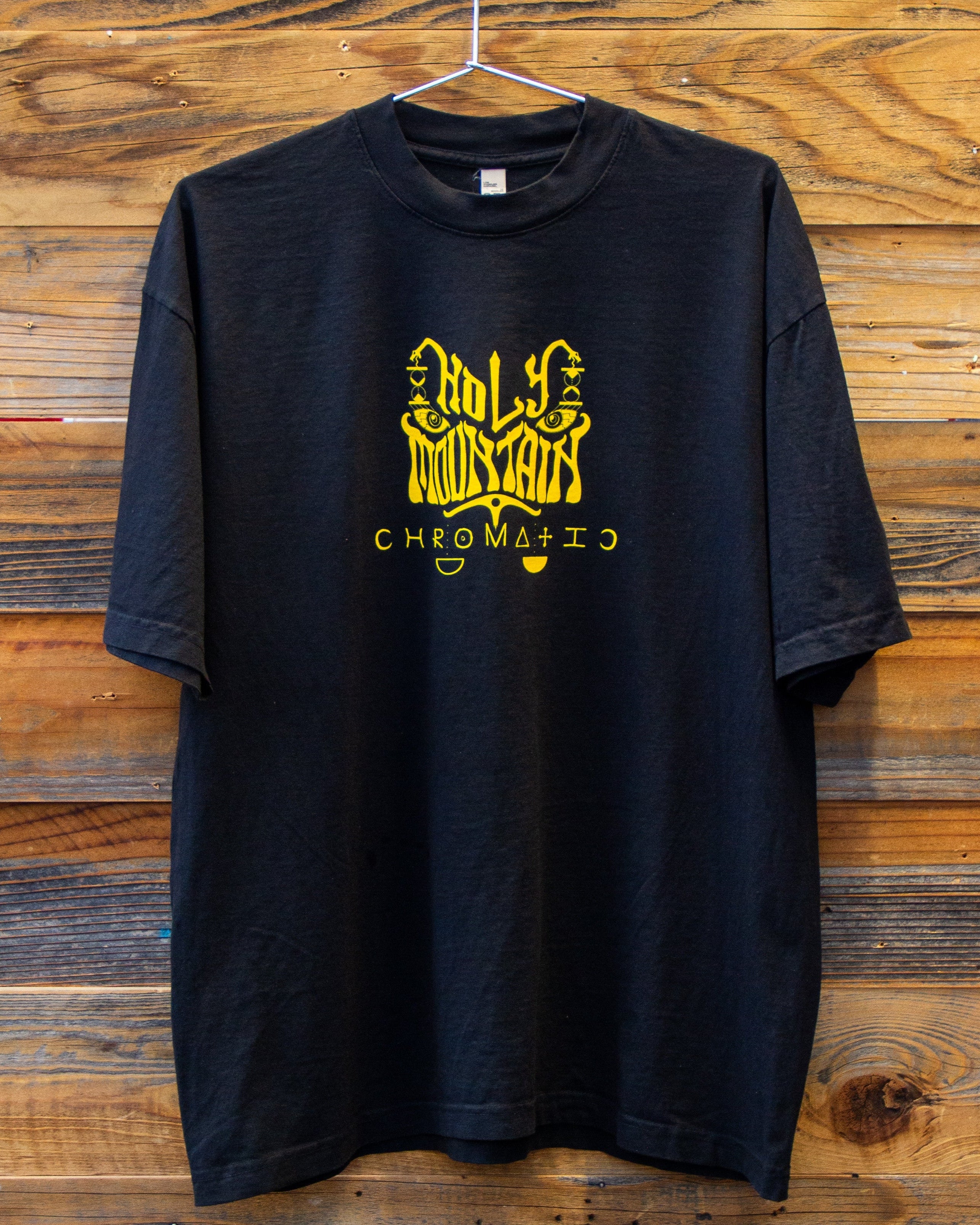 Holy Mountain Shirt Chromatic Coffee Black t shirt with yellow logo on a wooden background
