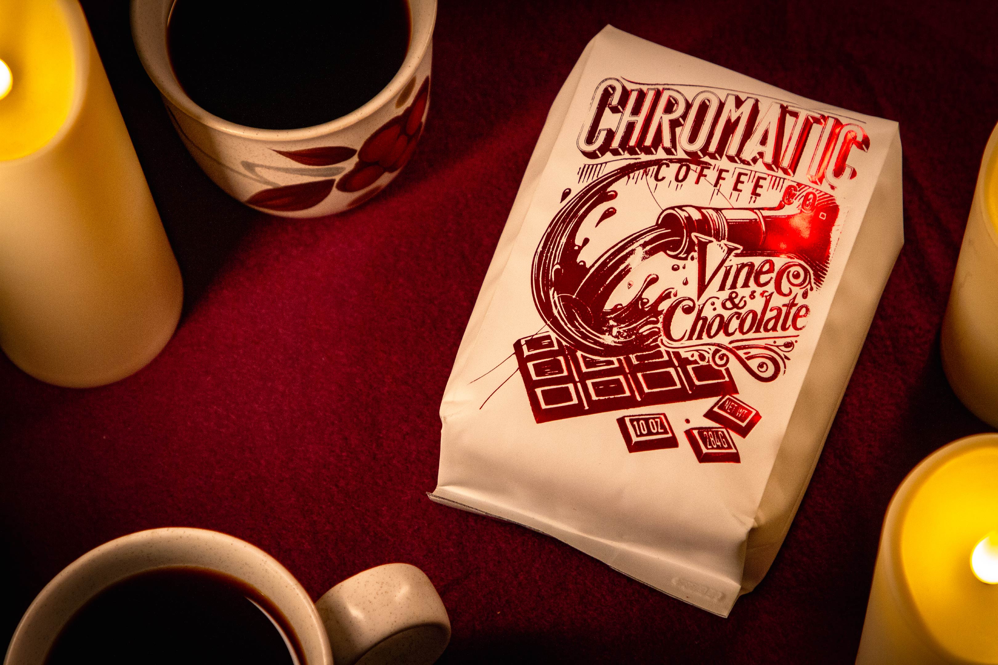 Vine & Chocolate-Coffee-Chromatic Coffee-Velvet Table Cloth with chocolate-themed design on a red surface with coffee cups and candles.